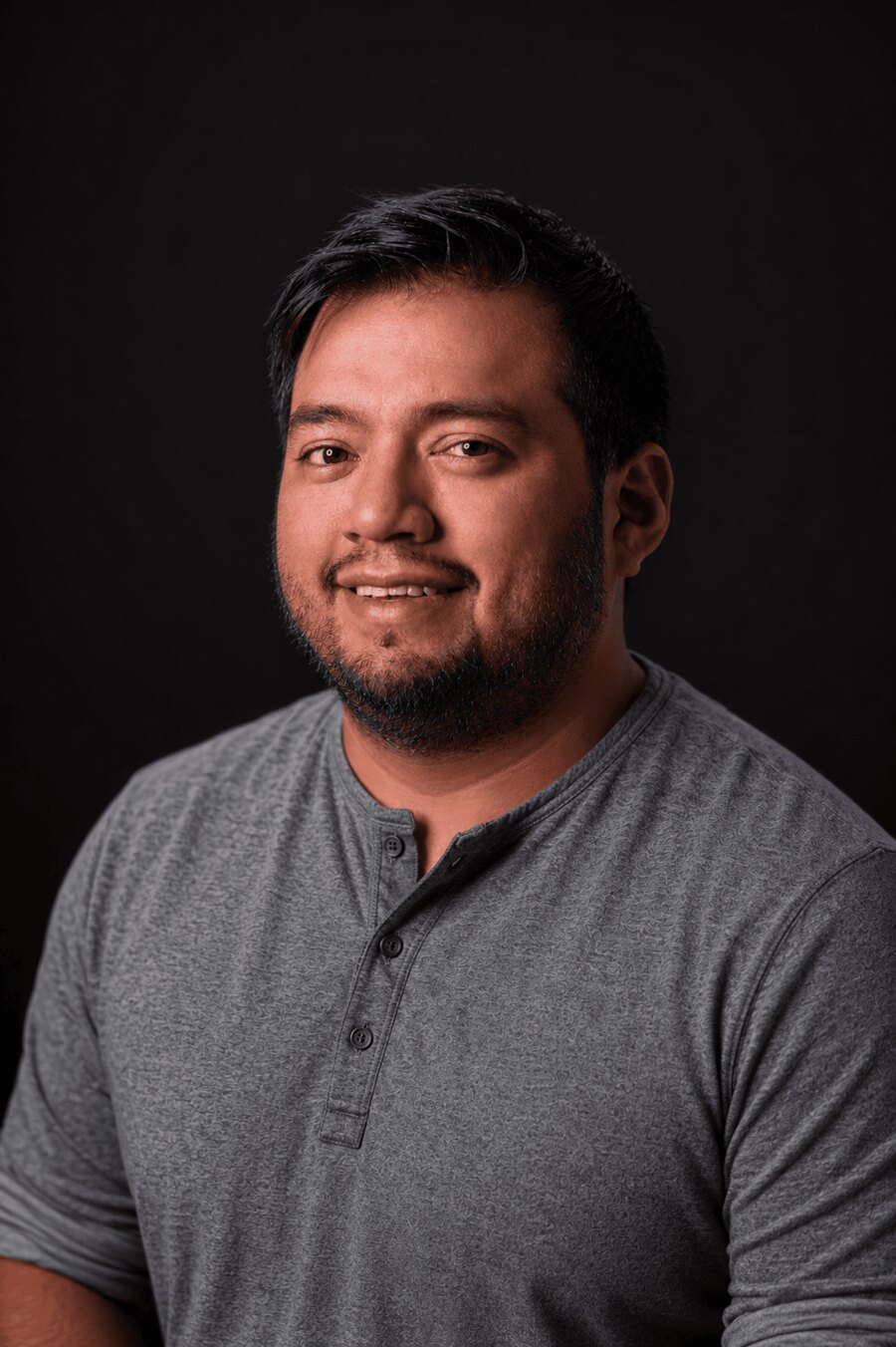 Portrait of Ricky Sunay — smiling, in a gray henley against a dark background.